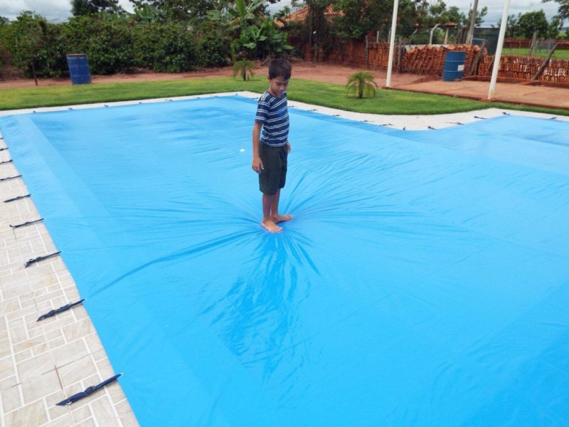 Criança andando sobre capa de proteção que cobre a piscina