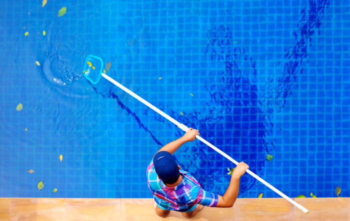 Homem limpando a piscina com peneira e cabo.