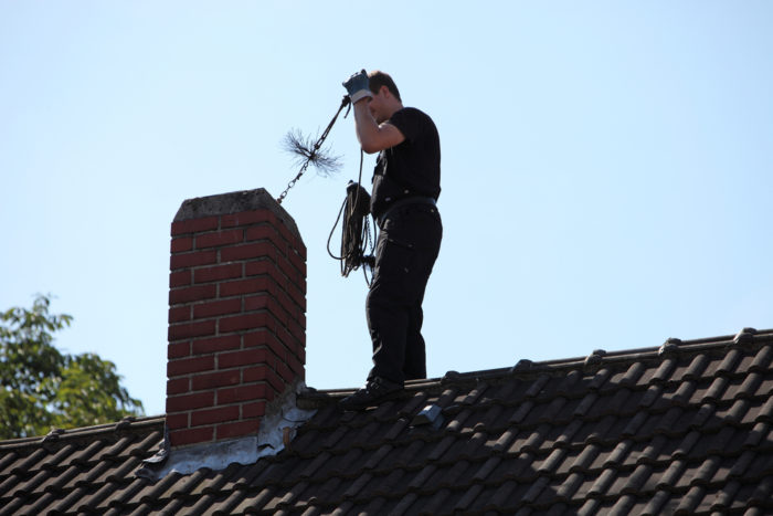 Homem sobre o telhado limpando a chaminé